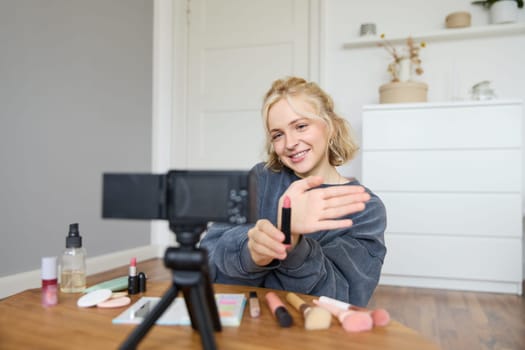 Portrait of young content maker, woman blogger recording a video on digital camera, showing lipstick colour to her followers, creating lifestyle vlog for social media account.