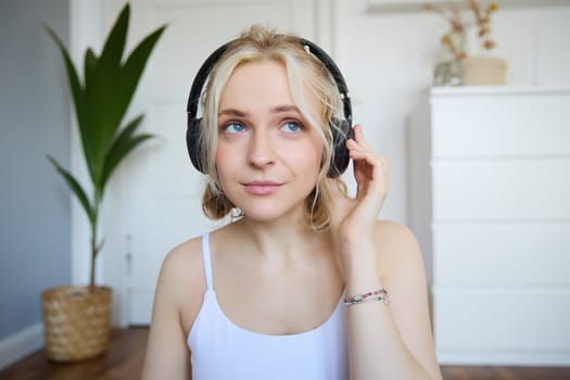 Concept of people and lifestyle, Close up of beautiful blond woman in wireless headphones, listens to music, enjoys good quality sound in new earphones.