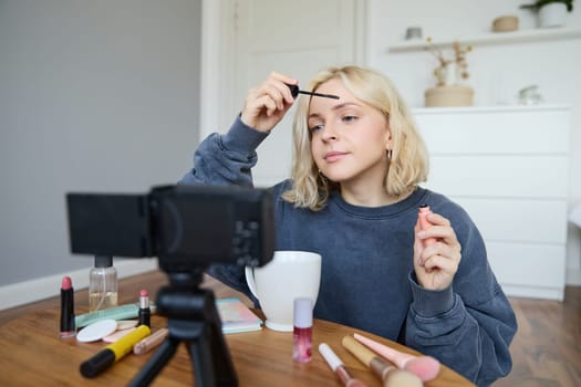 Portrait of blond smiling woman records a lifestyle blog, vlogger or makeup artist recording video for social media, holding mascara, reviewing beauty products for followers online.