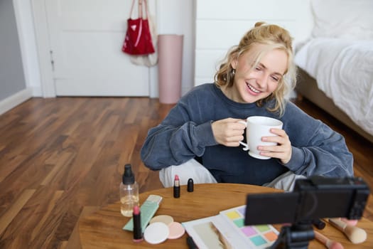 Portrait of young online influencer, social media blogger records new lifestyle video in her room, has digital camera connected to stabiliser, sitting in cosy space on floor, chatting about makeup.