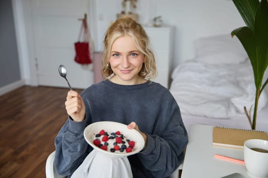 Portrait of young vlogger, content creator, showing her homemade breakfast on camera, eating dessert, smiling and looking happy.