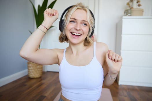Portrait of charismatic, beautiful young woman dancing and listening to music in wireless headphones, singing along favourite song in her room.