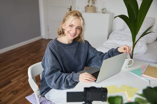 Portrait of young beautiful woman, social media influencer, recording video tutorial, lifestyle vlog, creating content in her room using digital camera.