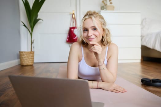 Portrait of young fitness woman, doing workout at home, looking at her gym instructor on laptop screen, doing online training session.