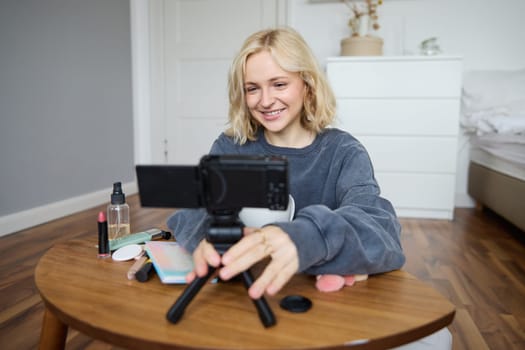 Portrait of young teenage girl in her room, recording a vlog, daily lifestyle video for social media, internet influencer advertising product online, talking to the camera, sitting on the floor.