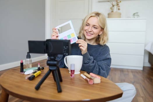 Portrait of beautiful smiling woman, recording video in her room, has camera on coffee table, reviewing makeup, doing lifestyle vlog for social media account, records a tutorial.