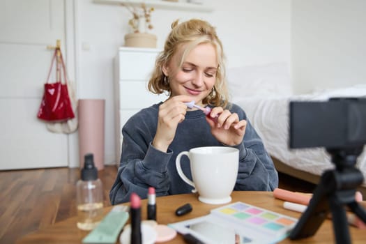 Image of happy, beautiful young social media influencer, female vlogger records a video on digital camera, tutorial on how to put makeup, getting ready for going out, talking to followers.