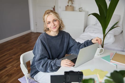 Portrait of young woman, lifestyle blogger, recording vlog video about her life and daily routine, sitting in front of laptop, talking to followers, sitting in her room.