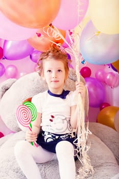 Funny little girl holding lollipops and bunch of balloons