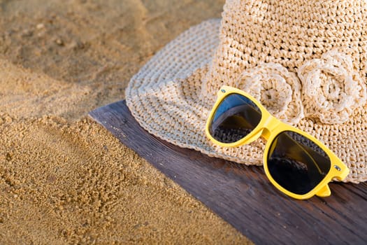 A summer hat and sunglasses lie on the sandy coast of the sea beach.