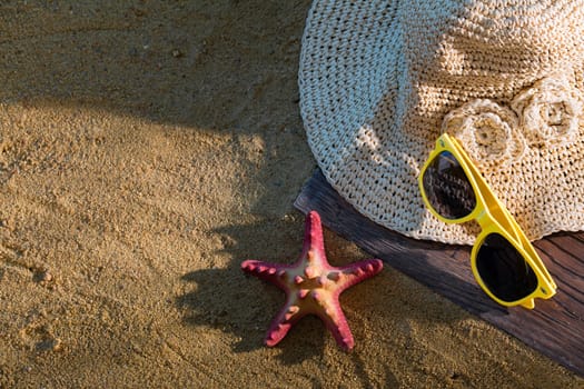 A summer hat and sunglasses lie on the sandy coast of the sea beach.