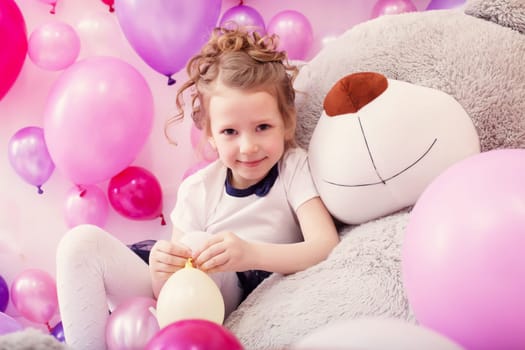 Smiling little girl sits leaning on big teddy bear