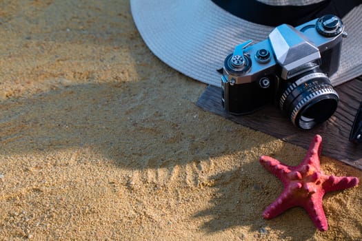 Old photographic film camera. Sunglasses. Sandy sea beach. Summer hat.
