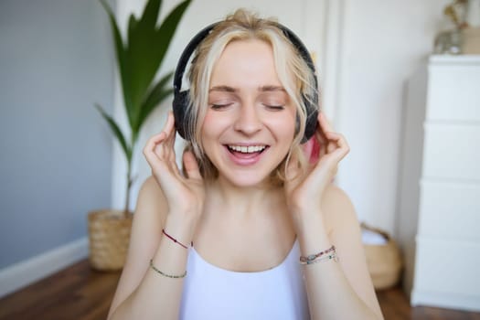 Close up portrait of woman smiling while listening to music in wireless headphones, singing with eyes closed.