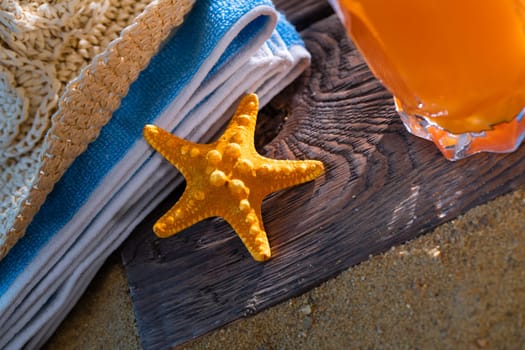 Fresh orange fruit juice stands in a glass with a straw. A beach towel lies on the sandy beach.