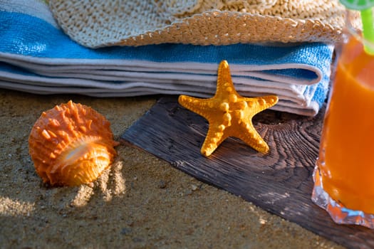 Fresh orange fruit juice stands in a glass with a straw. A beach towel lies on the sandy beach.