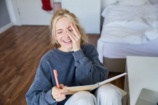 Portrait of charismatic blond girl, smiling woman in bedroom, holding notebook and pen, writing in journal or diary, creates to do list in planner.