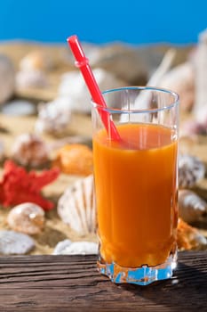 Fresh orange juice. A sandy beach on the shores of a cool sea. Brown platform board.