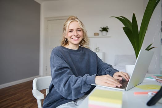 Portrait of young woman, student studying at home on remote education, working on laptop, typing on keyboard.