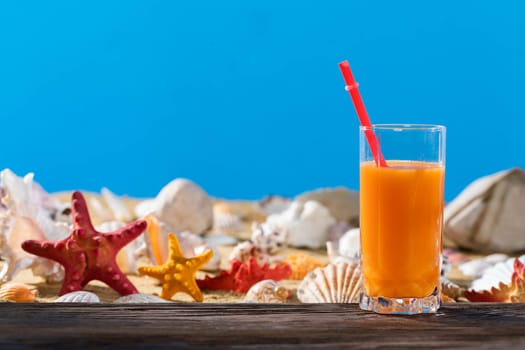 Fresh orange juice. A sandy beach on the shores of a cool sea. Brown platform board.