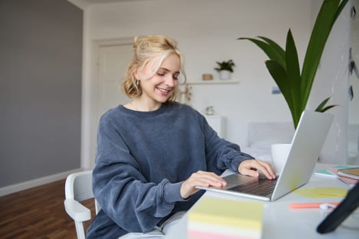 Portrait of young woman, student studying at home on remote education, working on laptop, typing on keyboard.