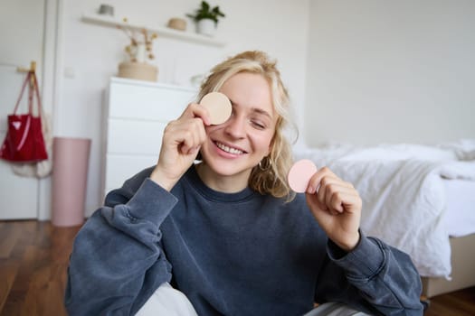 Close up portrait of happy, beautiful young vlogger, content maker recording video about makeup, showing beauty products on camera, smiling happily.