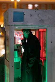 A man is talking on a phone in a booth. The booth is in a dimly lit area