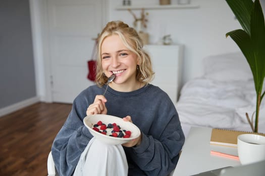 Portrait of young vlogger, content creator, showing her homemade breakfast on camera, eating dessert, smiling and looking happy.