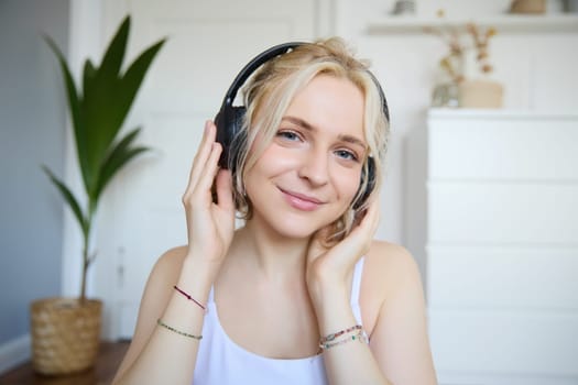 Concept of people and lifestyle, Close up of beautiful blond woman in wireless headphones, listens to music, enjoys good quality sound in new earphones.