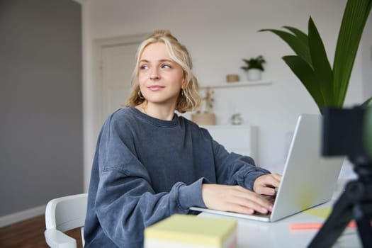 Portrait of smiling young woman, college student sits in her room, does homework, studies remotely from home, uses laptop for freelance work.