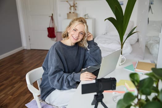 Portrait of young beautiful woman, social media influencer, recording video tutorial, lifestyle vlog, creating content in her room using digital camera.