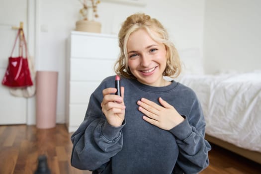 Portrait of young beautiful woman, content maker creating a new vlog, beauty video, showing lipstick, recommending makeup, records a tutorial.