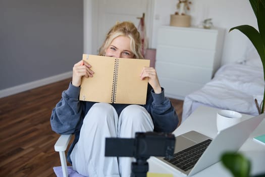 Portrait of cute, smiling young social media content creator, girl records video on digital camera and stabiliser, holds notebook, talks to audience, vlogging in her room.