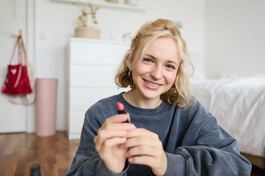 Portrait of young beautiful woman, content maker creating a new vlog, beauty video, showing lipstick, recommending makeup, records a tutorial.