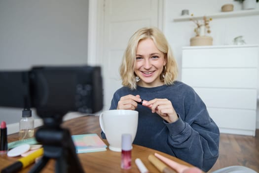 Portrait of blond smiling woman records a lifestyle blog, vlogger or makeup artist recording video for social media, holding mascara, reviewing beauty products for followers online.