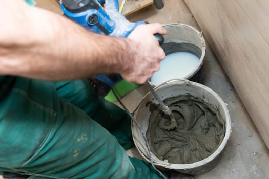 A construction worker mixes a special tile adhesive. Dense cement-based adhesive mixer.