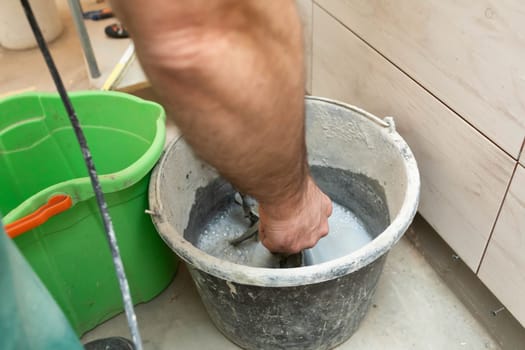 Cleaning of construction tools. Dirty water in a bucket. The builder washes the metal propeller of an electric mixer.