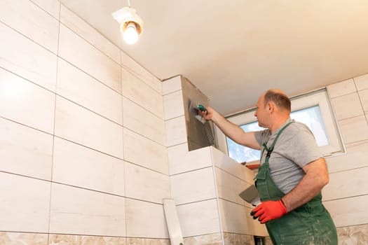 Applying cement glue to the wall with a special stainless steel trowel with teeth. An experienced construction worker.