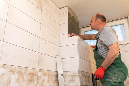 A middle-aged employee deals with laying tiles on the wall in the bathroom. An experienced construction worker.