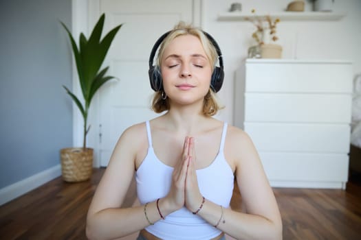 Wellbeing and people concept. Close up portrait of young woman in headphones, meditating, practice yoga, listens to podcast in earphones.