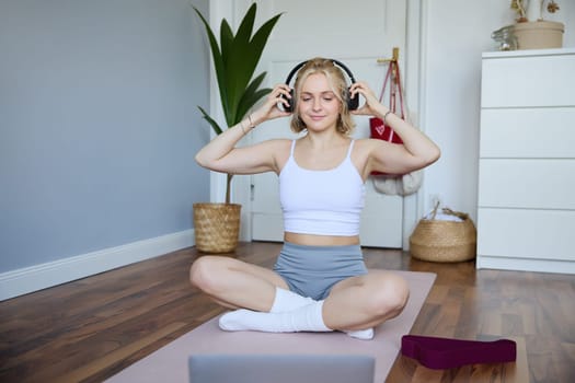 Portrait of fit and healthy young woman in wireless headphones, does workout, using online video tutorials, listens to fitness instructor on laptop, exercising at home.