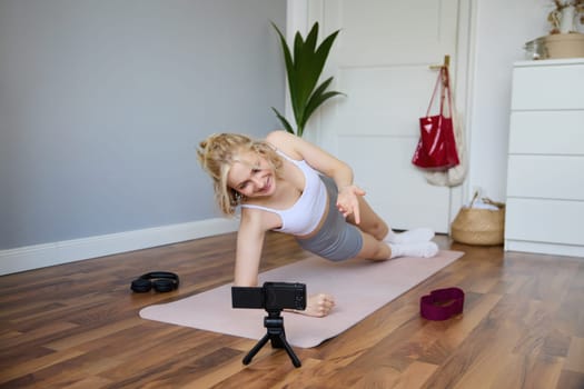 Portrait of fit and healthy young vlogger, fitness instructor woman standing in side plank, recording online lesson for clients on digital camera, shooting video about workout.