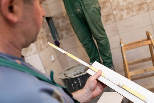 The builder measures the distance on the ceramic tile using a measuring tape. Distance measurement while the tiler is working.