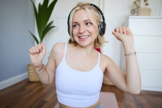 Portrait of beautiful blond girl, fitness woman dancing in wireless headphones, enjoying working out tuning into favourite song.