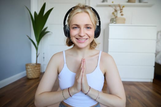 Wellbeing and people concept. Close up portrait of young woman in headphones, meditating, practice yoga, listens to podcast in earphones.