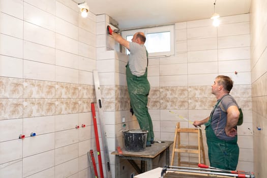 A middle-aged employee deals with laying tiles on the wall in the bathroom. An experienced construction worker.