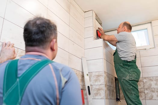 A middle-aged employee deals with laying tiles on the wall in the bathroom. An experienced construction worker.