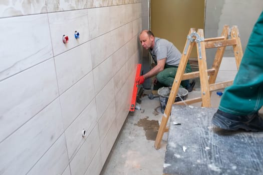 Using a spirit level, the employee checks the plumb and evenness of the entire plane of the glaze placed on the bathroom wall.
