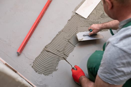 Professional construction worker laying ceramic tiles on the floor in the bathroom room.