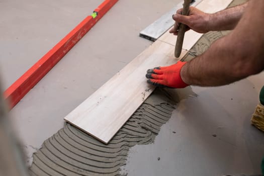 Rubber hammer. An experienced construction worker. Laying terracotta in the bathroom. Work clothes. He knocks with a hammer.